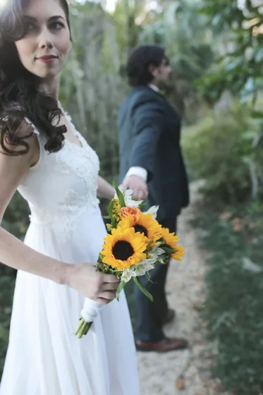A real wedding photo of a bride holding sunflowers with the groom behind her